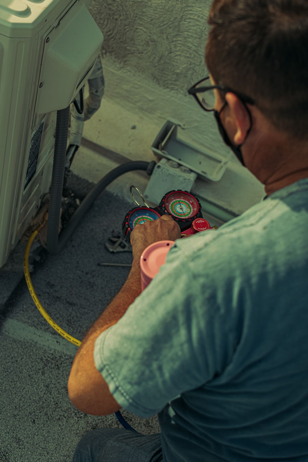 Technician servicing an outdoor air conditioning unit with pressure gauges